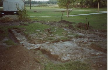 Excavated foundation outline in a grassy yard near a house.