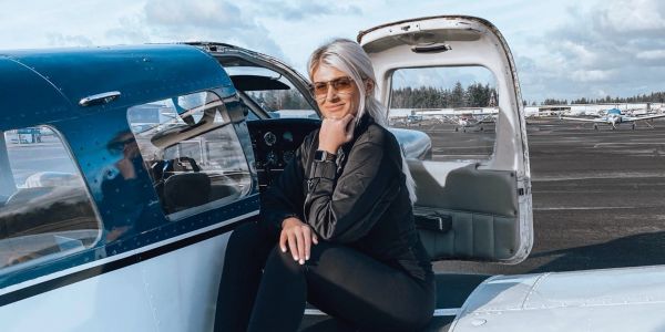 Woman pilot sitting on a small airplane wing at the airport.