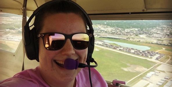Person smiling inside a small airplane wearing sunglasses and a headset.
