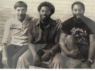 Three men sitting together, smiling, in a vintage black-and-white photo.