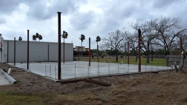 Construction site with metal beams and concrete foundation under cloudy sky.