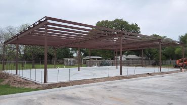 Steel frame structure with concrete foundation under construction in an open area.