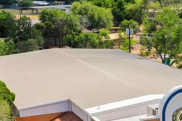 A large, flat grey roof surrounded by green trees and buildings.