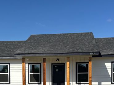 Modern house with black roof and wooden pillars under clear blue sky.