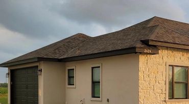 Modern suburban house with beige walls and dark roof under cloudy sky.