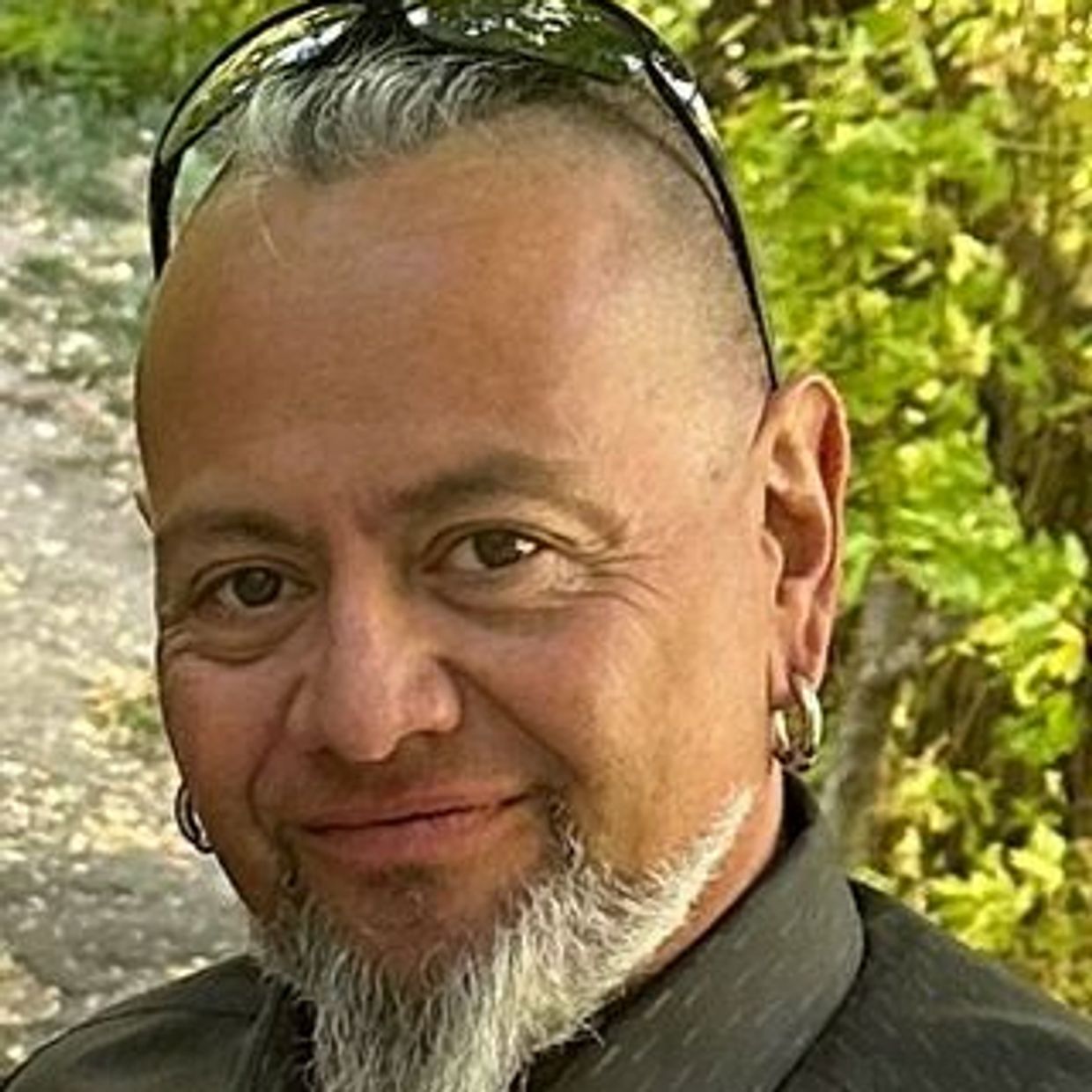 Smiling man with gray beard and earrings outdoors.