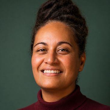 Smiling woman with natural hair and maroon turtleneck against green background.