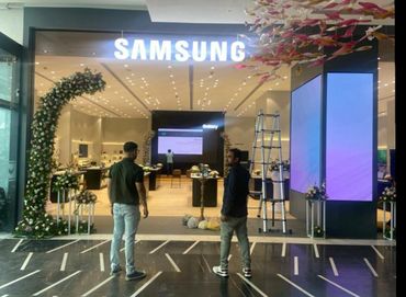 Two men stand outside a decorated Samsung store entrance.