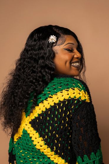 Smiling woman with curly hair and daisy hairpin wearing a colorful crocheted garment.