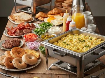 A breakfast buffet with scrambled eggs, bagels, bacon, and condiments.
