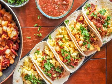 Breakfast tacos with scrambled eggs, potatoes, chorizo, and salsa on a wooden table.