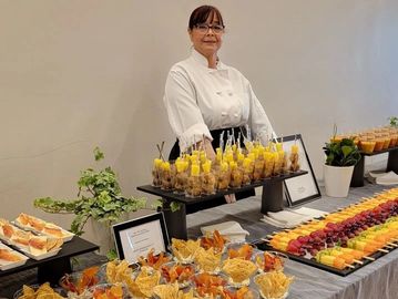 Chef presenting a beautifully arranged table with various appetizers and fruit skewers.