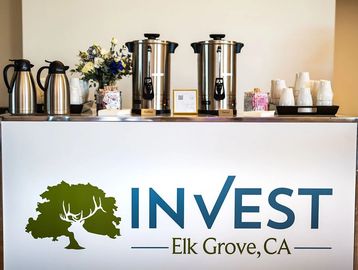 Coffee station setup with Invest Elk Grove branding and floral decoration.