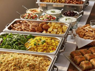A diverse Mediterranean buffet with grilled meats, salads, rice, pita bread, and baklava.
