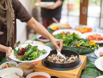 Person serving a healthy meal with greens and grains at a buffet.