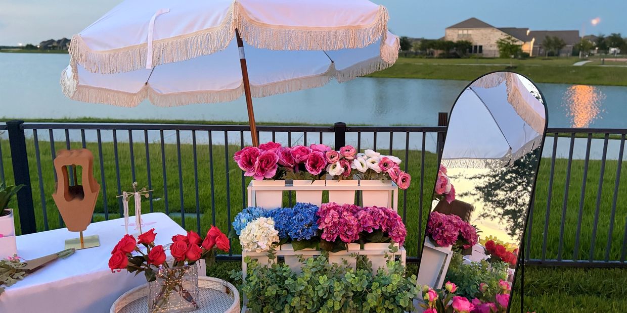 Colorful flowers displayed outdoors with a white umbrella and a mirror reflecting the scene.