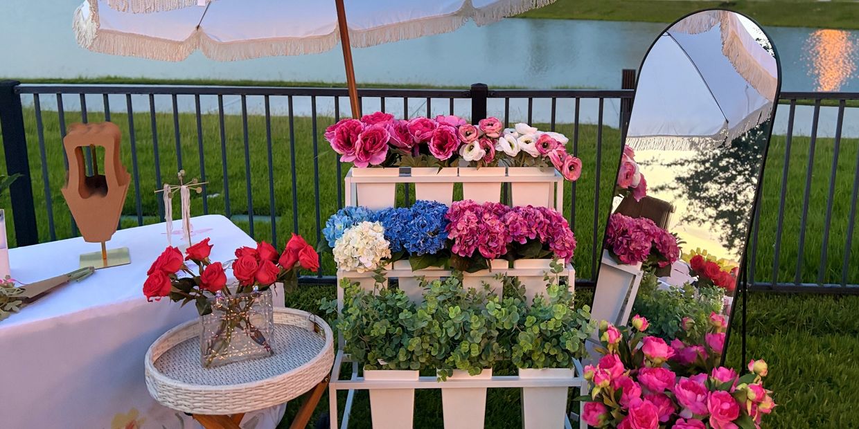 Colorful flowers displayed outdoors with a white umbrella and a mirror reflecting the scene.
