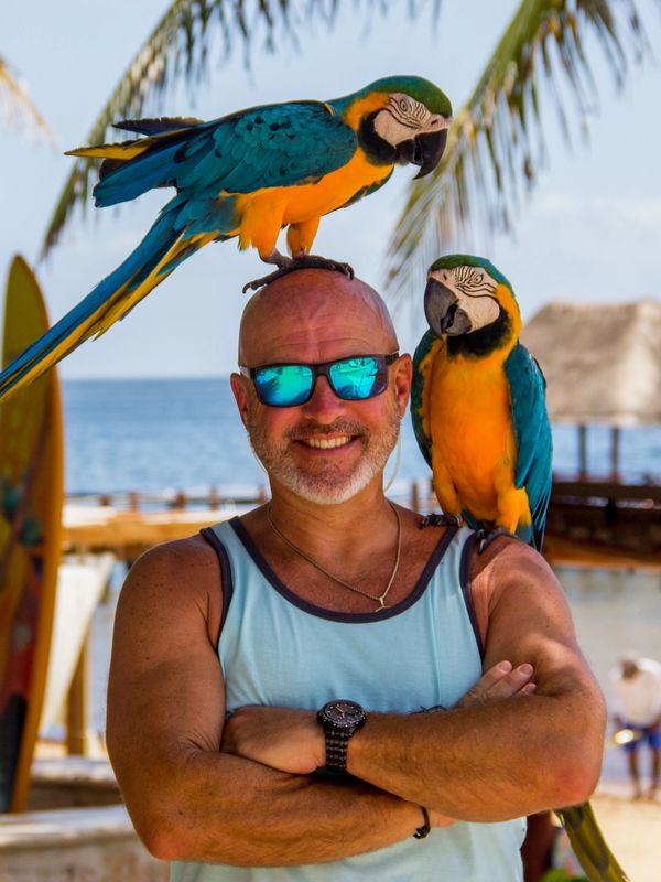 Robert McGuigan with 1 parrot on shoulder and one on head
