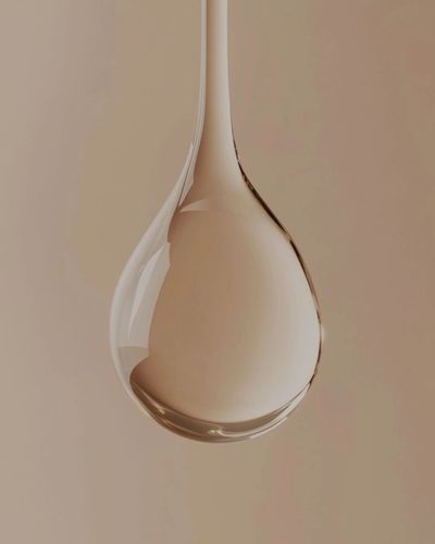 Close-up of a single transparent water droplet against a beige background.