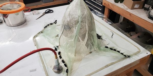 A translucent mold setup on a workbench with clamps and a red hose attached.