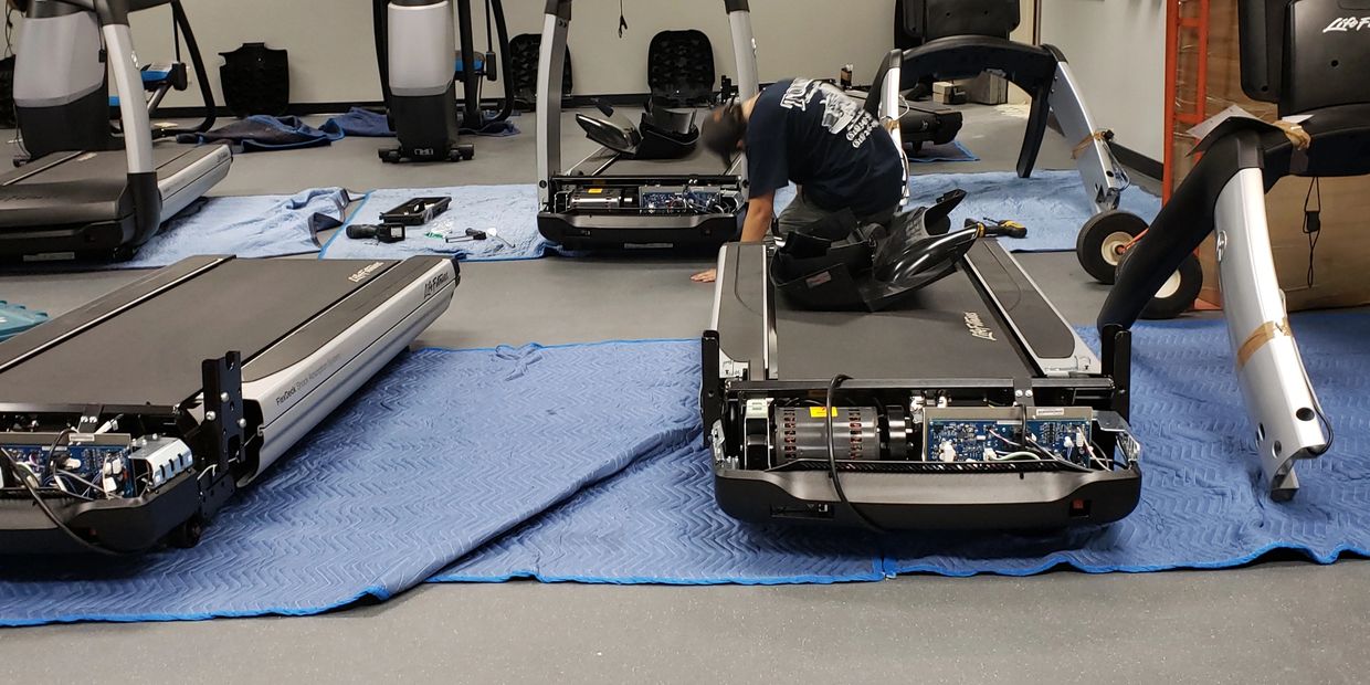 Person repairing treadmills in a gym.