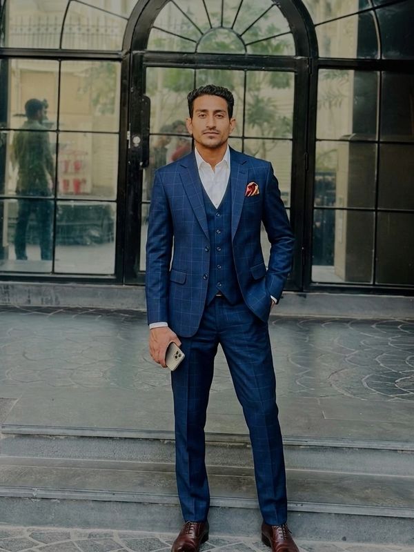A man in a blue three-piece suit stands confidently on steps, holding a phone.