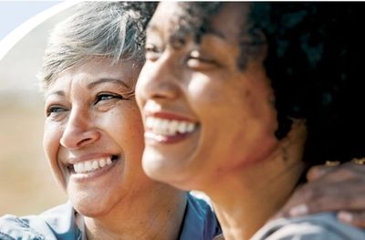 Two women smiling warmly, enjoying a happy moment together.
