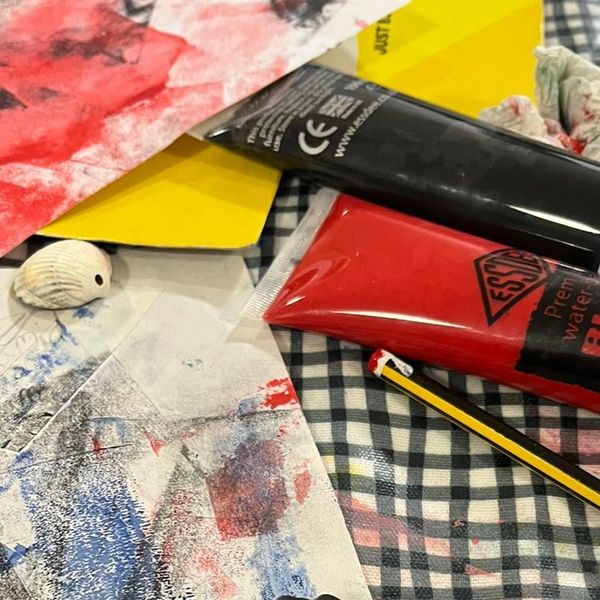An Ink roller, black and red printing inks and a pencil are scattered on a table.