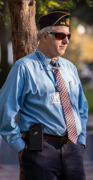 Veteran in official attire leaning against a tree outdoors.