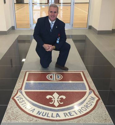 Man in suit kneeling next to a shield emblem on the floor.