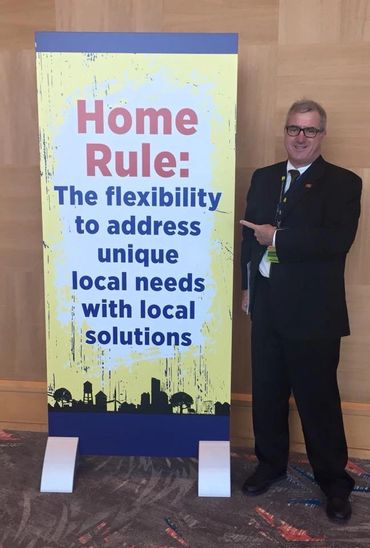 Man in suit pointing at a sign about home rule and local solutions.