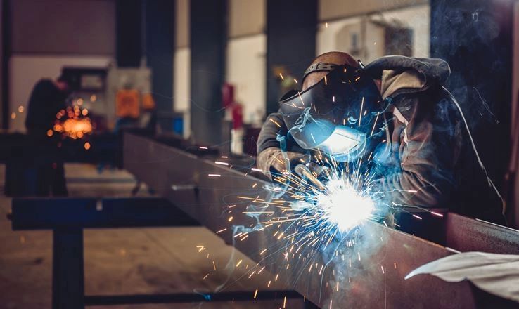 Welder sparks flying as they work on metal beam in industrial workshop.