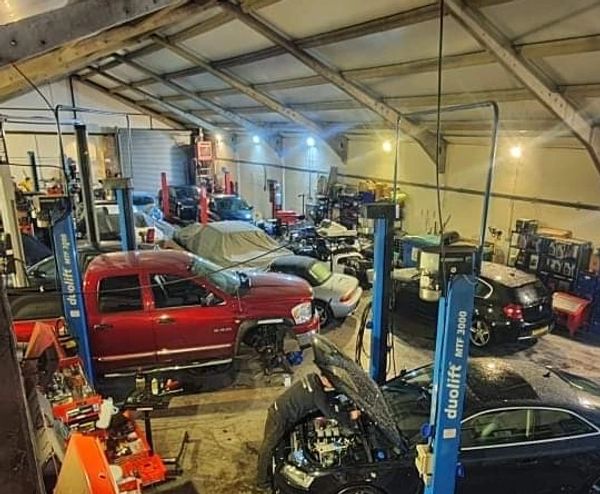 Busy auto repair shop with multiple cars and a mechanic working on an engine.