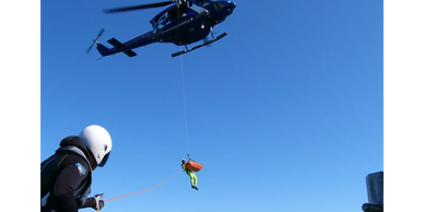 Helicopter rescue operation with a person being lifted while another assists below.