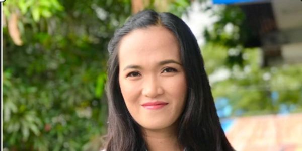 A woman with long black hair smiles outdoors in a floral blouse.