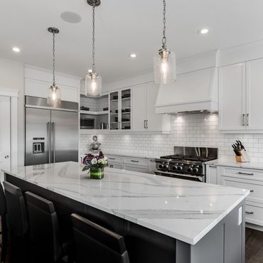 Modern white kitchen with marble island and pendant lights.