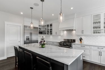 Modern white kitchen with marble island and pendant lights.