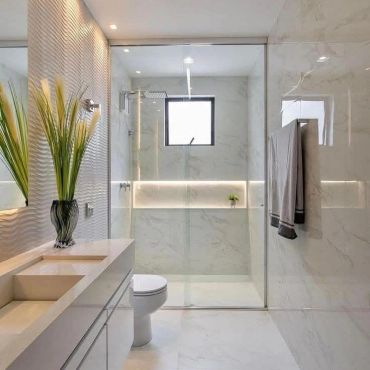 Modern bathroom with marble walls, glass shower, and elegant vase.