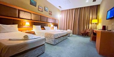 Hotel room with three beds and warm lighting.