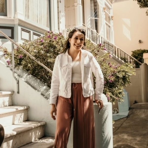 A woman smiling outdoors near a staircase and flowering bushes.