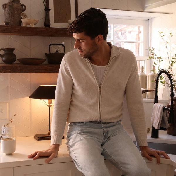 Man sitting on kitchen counter in cozy beige sweater and jeans.