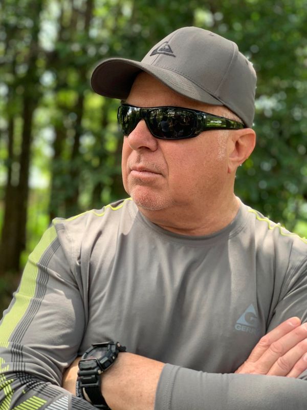 Man in gray sportswear and cap wearing dark sunglasses outdoors.