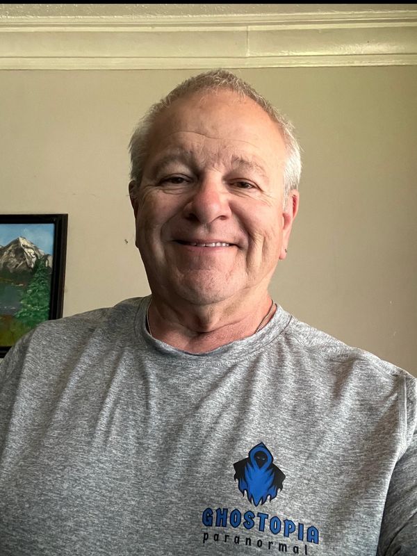 A smiling man wearing a grey Ghostopia Paranormal t-shirt.