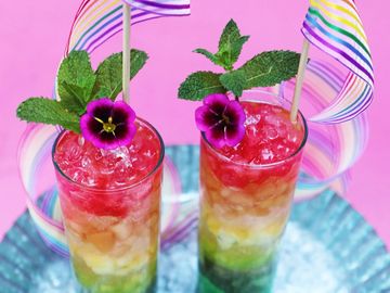 Two colorful rainbow cocktails garnished with mint and edible flowers.