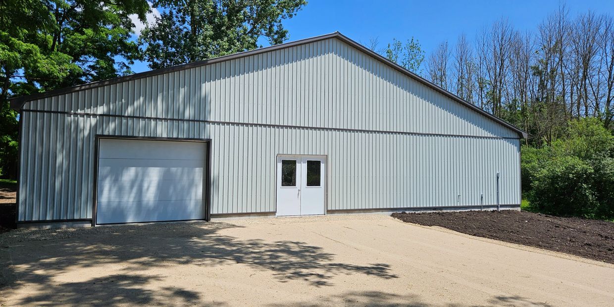 Large metal building with garage and double doors surrounded by trees.