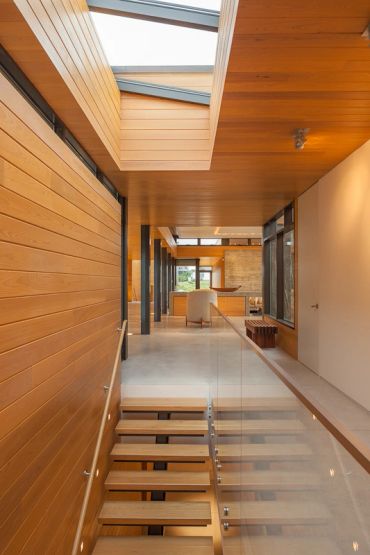 Modern wooden staircase with glass railing and skylights.