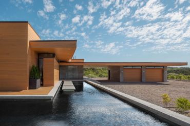 Modern house with a water feature and garage under a partly cloudy sky.