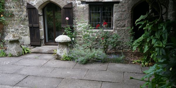Stone cottage entrance with wooden shutters and garden mushrooms.