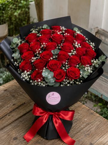Elegant bouquet of vibrant red roses wrapped in black paper with a red ribbon.