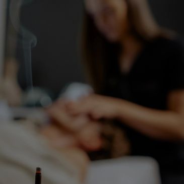 A person receiving a facial massage in a spa setting with incense burning.
